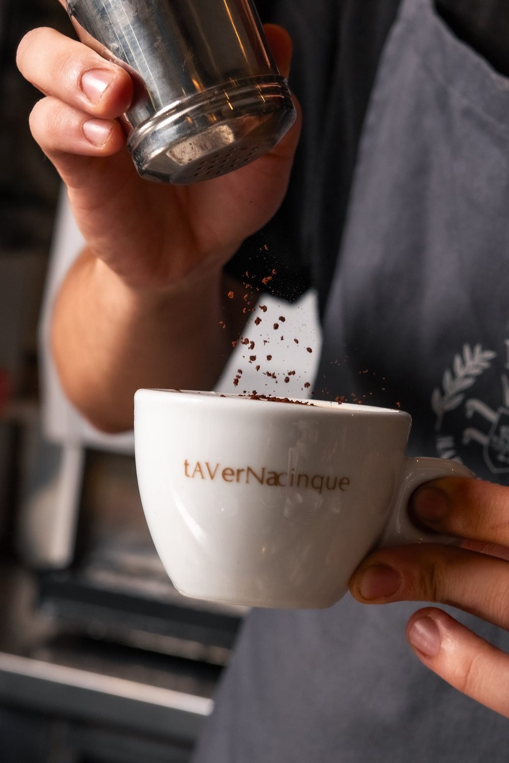 Una spolverata di cacao su un cappuccino, nella tazza con il logo Tavernacinque